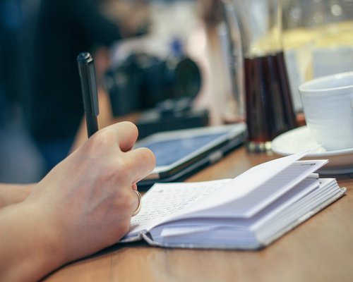 person writing in journal over coffee